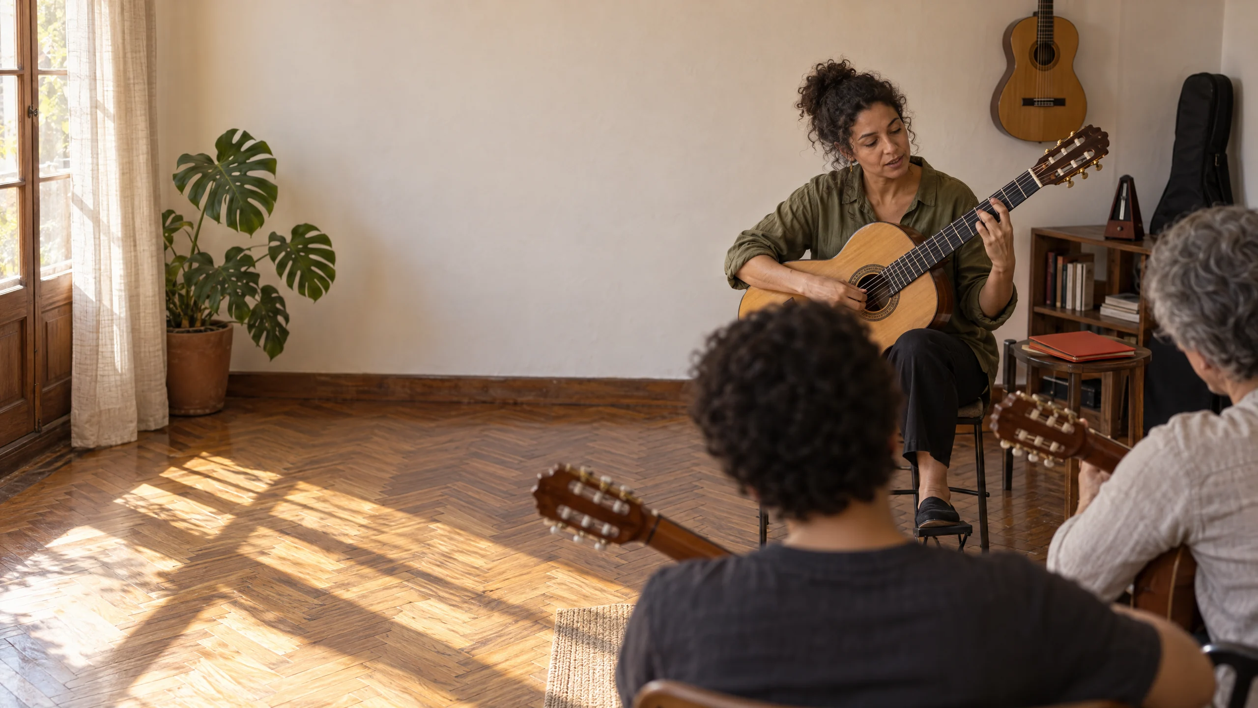 Professora de violão tocando o acorde para a turma presencial, com dois alunos de costas, cada um com o próprio violão.